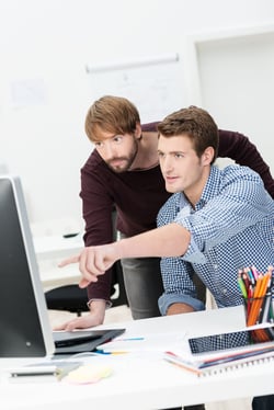 Businessman pointing to his computer monitor showing his partner something on the screen as they work together in the office
