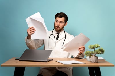 serious-doctor-looking-at-his-documents-while-sitt-2024-10-18-09-52-49-utc